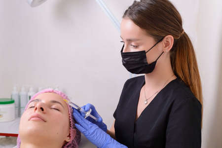 portrait in the cosmetologists office. A young girl in a medical suit, gloves and a syringe performs...