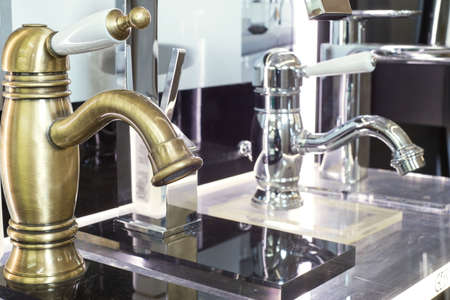 a variety of faucets taps on a white shelf in a shop counter. Close-up of faucets for faucet sink,...