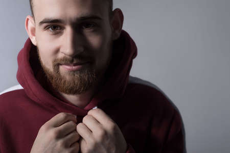 closeup, dramatic portrait of a handsome bearded guy of twenty five years old, in a red warm sweater with a hood, holding hands, tightening the ropes.の写真素材