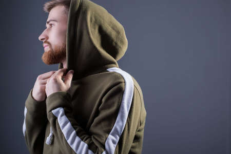 a young bearded guy of twenty-five years old. in a sports jacket with a swamp-colored hood. On a...