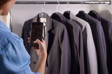 girl using a smartphone photographs a counter with quality business jackets in a clothing storeの写真素材