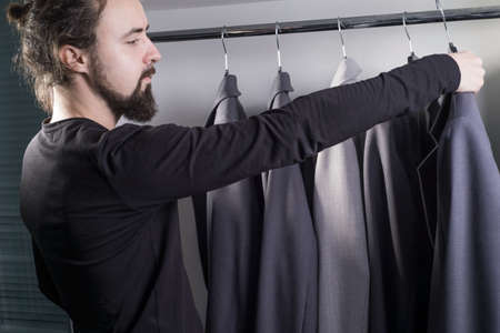 Closeup portrait of a young bearded guy, millennial, in a men's clothing store chooses a business suit for work. Sale of men's clothing. business jacketの写真素材