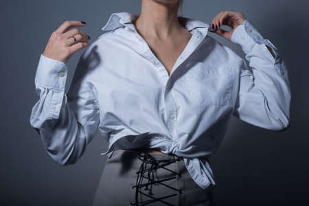 close-up. a young girl in a white shirt and a gray designer skirt with ornamental lace. On a gray background. Promotional photo for the catalog. Fashionable photo of a female look. Modern fashion trends and options for wearing a shirt with a skirtの写真素材