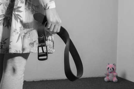 Child abuse concept. A girl in a colored dress sits in a corner, covers her face with her hands, holds a belt next to her father to beat a child. A girl with pigtails is crying. Violence in family. Father beats raping daughter. Disassembly of parents with childrenの写真素材