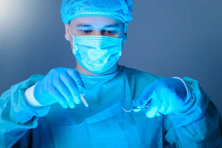 close-up portrait of a caucasian doctor surgeon, in a sterile suit, mask, holding a scalpel and...