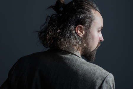 Studio dramatic portrait of a young bearded guy, thirty years old, with curly dirty greasy hair and a jacket. On a gray backgroundの写真素材
