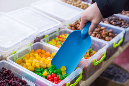 Dried kumquat. the seller, with the help of a spatula, picks up a multi-colored square meter from a...
