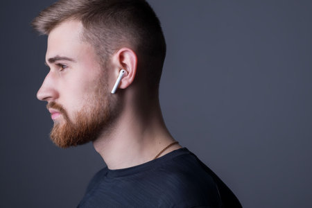 Closeup portrait of a young bearded guy of twenty-five years old, standing in profile. In wireless white headphones. Sporty styleの写真素材