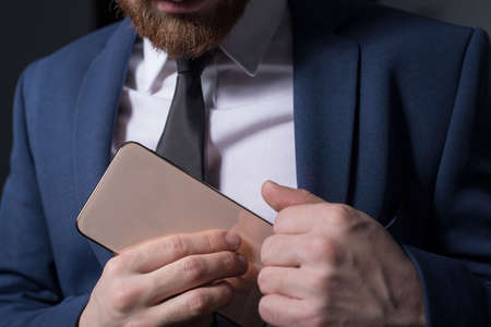 Close-up, studio dramatic portrait of a handsome bearded man, in a business suit, holding a new...