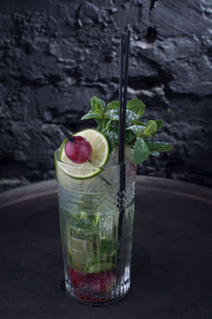 fresh coctail on the black background close-up, advertising shot of a light alcoholic cocktail, with a sprig of mint, icing sugar, with decorative grape berry. In a rustic style, on a dark background. An interesting advertisement for bright pictures. For catalogs and menus of alcoholic drinks, cocktails for parties. Dramatic light. Harmful alcoholic drink. Low alcohol drink. Light cocktailの写真素材