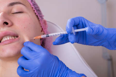 portrait in the cosmetologists office. A young girl in a medical suit, gloves and a syringe performs...