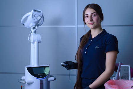 Zaporozhye. Ukraine. February 2020. A girl, a dentist, looks at the camera, smiling, holding in her hand the remote control of the Beyond dental treatment apparatus. Dentist girl wearing a blue polo t-shirt with Lacosteのeditorial素材