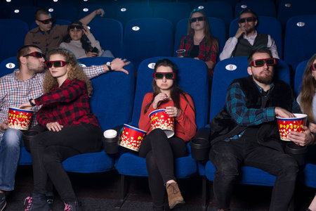Loving couples hugging while watching a movie, and only a lonely girl sadly takes possession of the sweets of celibate loneliness. a group of young people of different sexesの写真素材