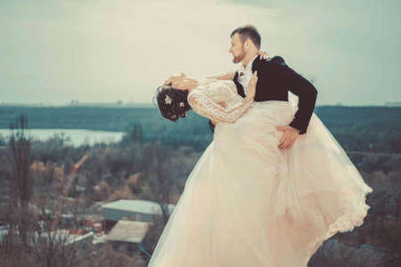 Runaway Bride. Wedding. Groom catches his bride. wedding photo of the bride and groom on the background of a river landscape sitting on a bench by a tree.の写真素材