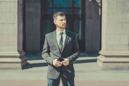 Portrait of a young bearded guy of twenty-five years old, in a business suit, against the background of an office building. Posing looking at the camera.の写真素材