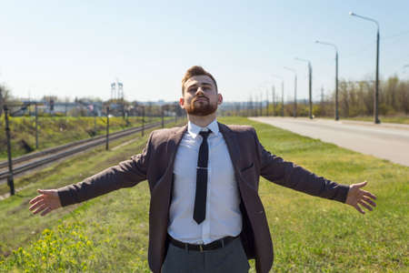 Young woman enjoying the fresh air. Portrait of a young guy of twenty-five years old, in a business suit, with open arms, against the background of empty traffic on a daytime streetの写真素材