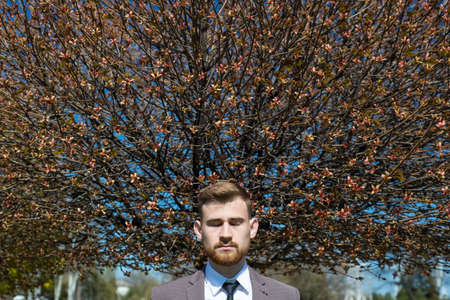 Portrait of a young bearded guy with closed eyes, from whose head a tree grows. on open air. In...