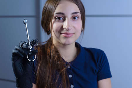 Closeup portrait of a female dentist doctor holding a refillable metal syringe for anesthesia in her hand. At the dental clinic. Anesthesia in dentistry. Needle with a syringe. Reducing plastic waste in dentistry. Toothache treatment.の写真素材