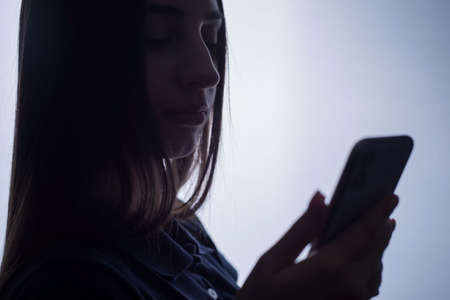 Studio portrait of a young girl of twenty-two, holding a new smartphone in her hand. The advertising photo is bright.の写真素材
