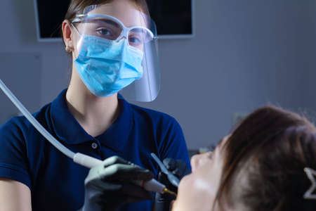 close-up, from an unusual angle, view, a dentist using dental equipment treats a patient a girl with...