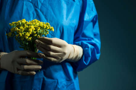 a doctor in a surgical suit and gloves, holding flowers in his hands. Medical concept. Yellow...