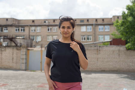 portrait of an Indian girl athlete, view from below, listens to music on headphones, against a...