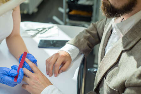 Woman giving man a manicure manicure a young girl manicures a man of thirty years in a business suit. The beauty of nails in men. Manicure salonの写真素材