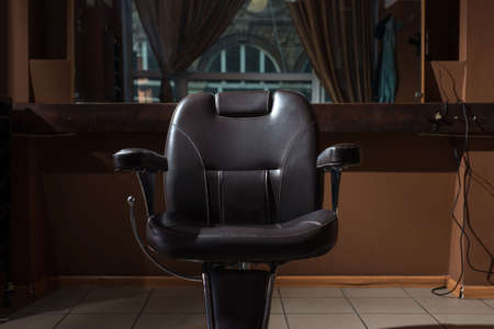 a hairdressing chair made of brown leather, under a ray of light, in a barbershop, a hairdressing salon. Close-up, barbershop interior. Hair cutting, shaving, hair careの写真素材