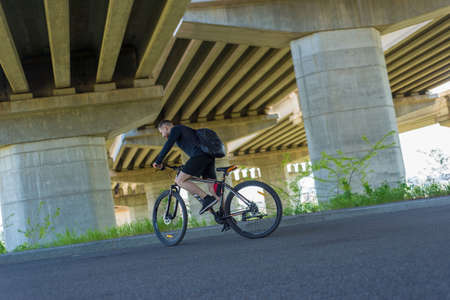 athlete, bearded guy cyclist, rides on the highway on a sports bike. Under the bridge. Outdoors. Spring sports.の写真素材