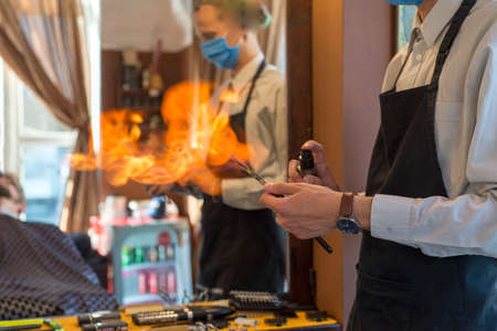 Professional male hairdresser heating the blade of old-fashioned straight razor under stream of fire...