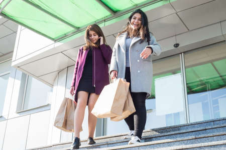 two beautiful smiling Indian girls sisters, with eco shopping bags, amid the hypermarket, go down...