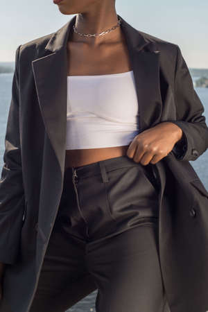Young african fashionable business woman in a business black suit jacket and trousers posing showing details of a suit. Against the background of blue sky. Business fashion style in a black suit, on a black girl. African girl business styleの写真素材