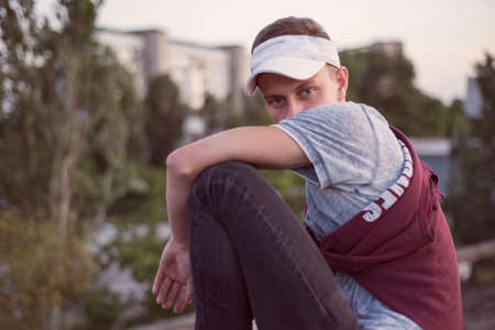 Portrait of a young guy sitting on the roof. Against the backdrop of the setting sun. Looks into the...