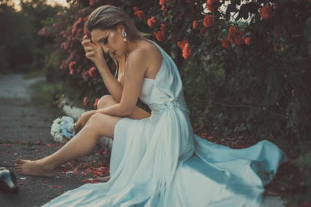 sad bride smokes a cigarette and drinks alcohol. Against the background of a floral background of roses. Sad bride smoking a cigarette, with a bottle of alcohol in her handの写真素材