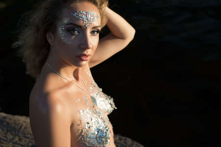 nude body art girl closeup portrait, on black background. Young beautiful girl of twenty-nine years old, looking at the camera, with body art makeup, silverの写真素材