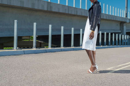African fashion model, in black leather jacket, white dress, posing. Against the background of...