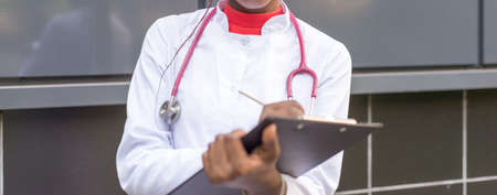 Afro American female doctor, twenty-seven years old, in a white coat, with a phonendoscope, writes a...