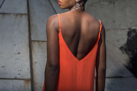 African girl in an orange dress, from the back, on a background of street texture. Black model girl posing, African fashion, orange dress.の写真素材