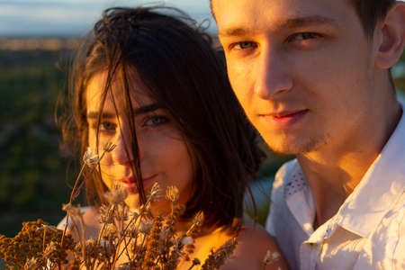 close-up portrait of a guy with a girl, against the backdrop of the setting sun, summer evening. guy with a girl, a young couple of twenty two years old, hugging. romantic love couple Happy couple breathing fresh air in a colorful field with red poppy flowersの写真素材