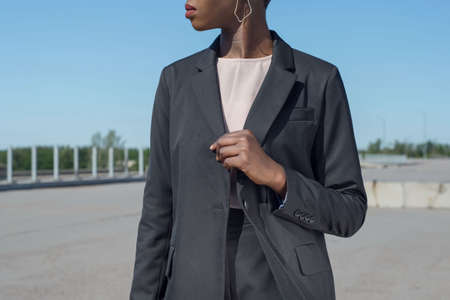 Young african fashionable business woman in a business black suit jacket and trousers posing showing...