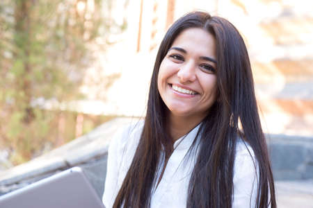 Portrait of a smiling, biting Indian girl. In the open air, holds the tablet