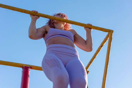 young sportswoman pulls herself up on the horizontal bar. Outdoort. Warkout Girl on street workout....