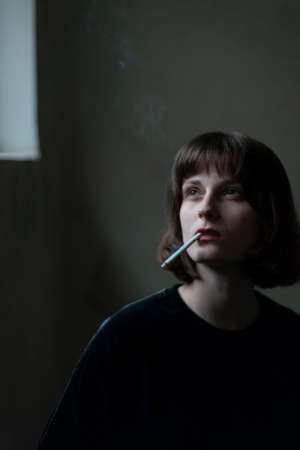 Portrait of a young beautiful girl of generation Z smoking a cigarette at the entrance of the house.