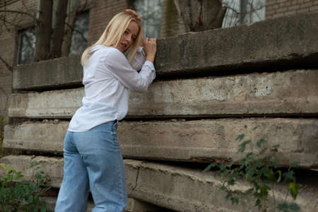 portrait of a young beautiful blonde girl standing by a concrete slab in the street a beautiful young girl sitting sadlyの写真素材