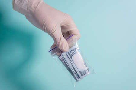 money in a protective bag, holds a hand in a medical glove, on a blue background Hand in glove holds...