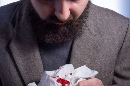 bloody cough, bearded businessman coughing up blood into a napkin, close-up, medical concept Close up from a man with bloody tissueの写真素材