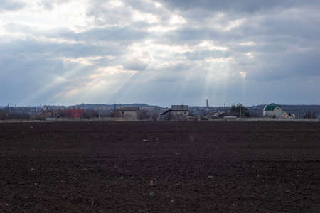 spring landscape of half-plowed field and green grass, against the backdrop of a cloudy sky