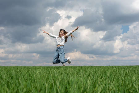 teen girl jumping in the green grass field, against the backdrop of the cloudy sky.の写真素材