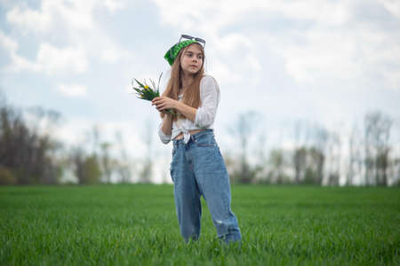 portrait of a fashionable little girl with a bouquet of wildflowers, in a green field, against a background of a cloudy sky.の写真素材