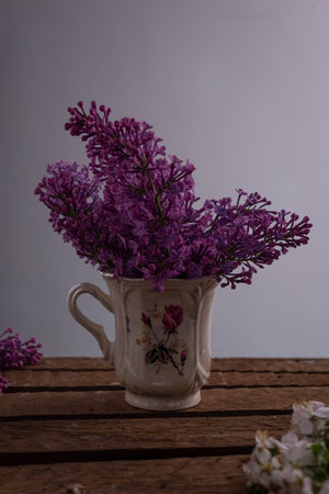 still life of lilac branches in a teacup, on a wooden table, on a gray background. Spring still life...